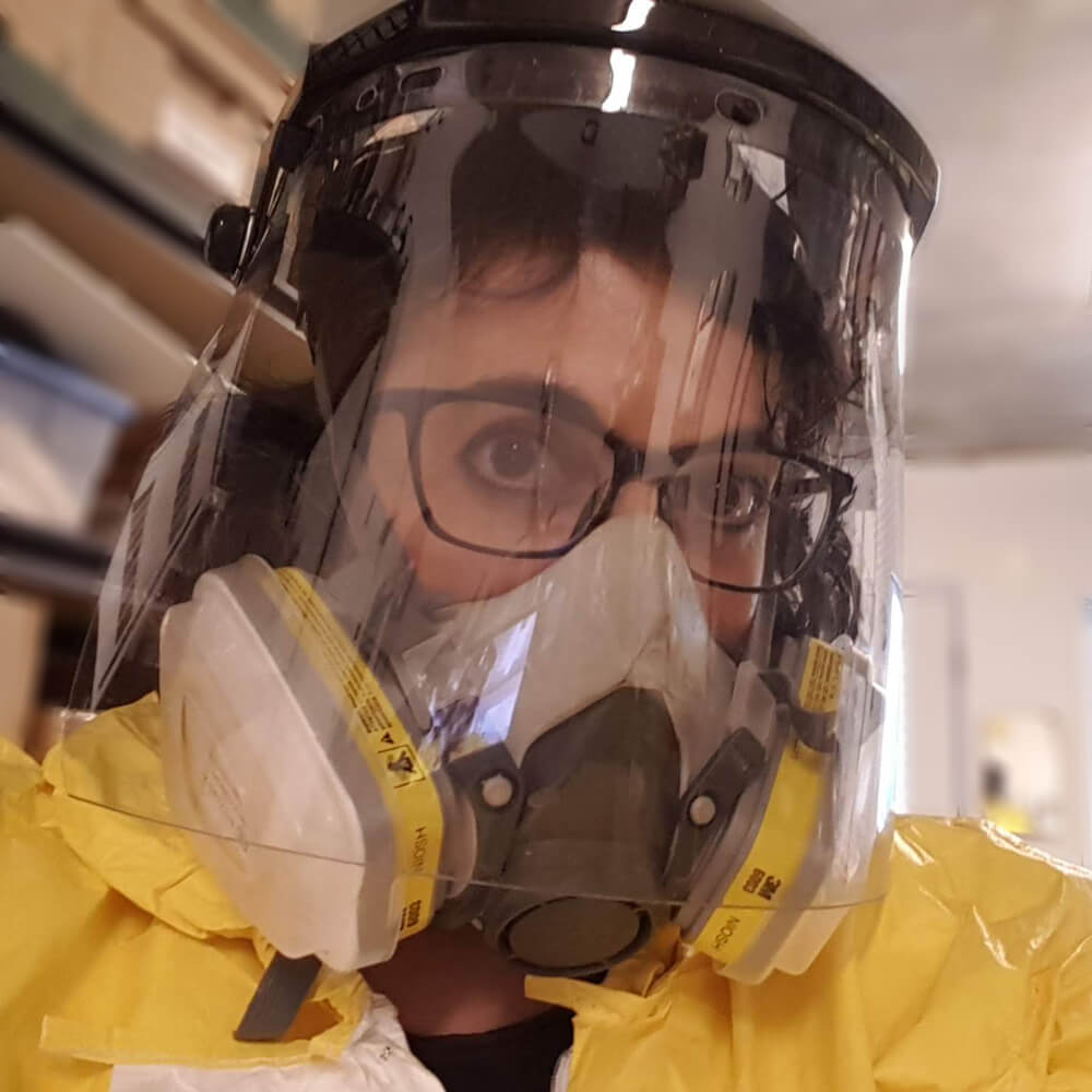 A photo of the artist wearing a respirator, face shield, and chemical resistant coveralls
